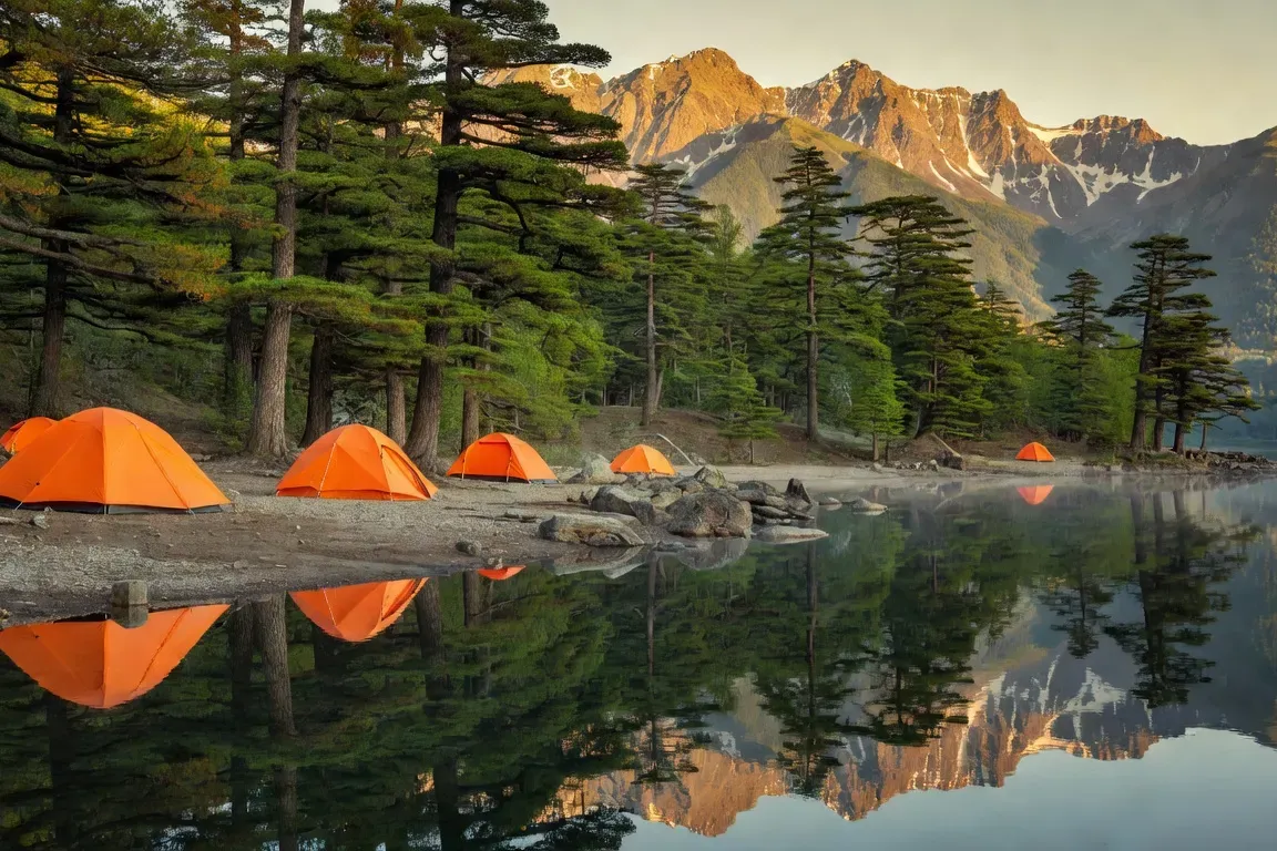 Campement au bord du lac Télétskoïe avec tentes orange et reflets de montagne